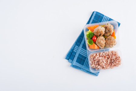 Thai style fried pork ball cooked by clean food concept with vegetables and brown rice in lunch box on white tableの写真素材