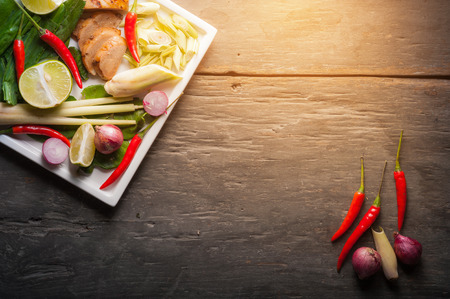 Ingredients set for Thai spicy soup (Tom-yum) include lemon, galangal, red chili, red onion, lemongrass, and kaffir lime leaf on wood table in low key morning scene with blank copyspace area for text or messageの写真素材