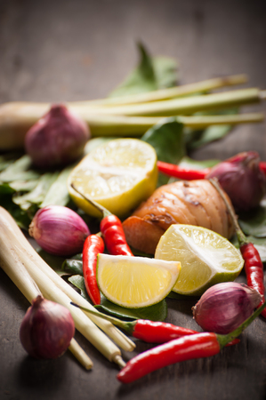 Ingredients set for Thai spicy soup (Tom-yum) include lemon, galangal, red chili, red onion, lemongrass, and kaffir lime leaf on wood table in morning sceneの写真素材