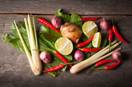 Ingredients set for Thai spicy soup (Tom-yum) include lemon, galangal, red chili, red onion, lemongrass, and kaffir lime leaf on wood table in morning sceneの写真素材