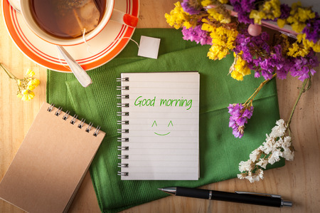 "Good morning" is written on opened notepad with pen and a cup of hot tea on wood table in cafe with morning sceneの写真素材