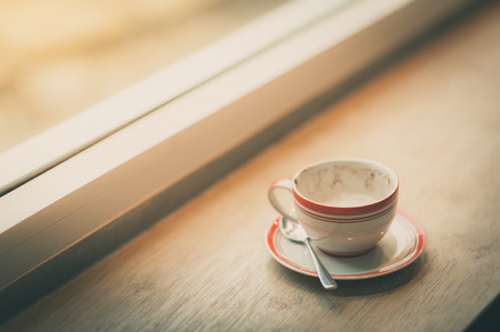 Coffee cup on wood bar beside window at coffee shop in afternoon time with film filter effect