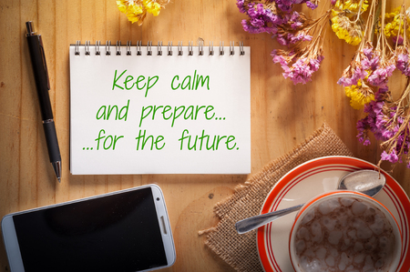 "Keep calm and prepare for the future" is written on notepad with pen, smart phone, and a cup of hot coffee on wood table in afternoon timeの写真素材