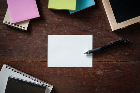 Blank paper with area for text or message, pen, notebook, and sticky paper on wood table with low key sceneの写真素材