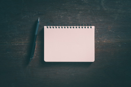 Small opened notepad with blank area for text or message and pen on rustic wood table with low key...