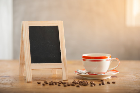 Small A-frame black board with blank area for text or message and coffee cup on wood table in morning timeの写真素材