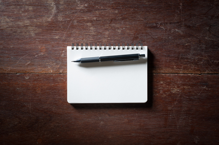 Small opened notepad with blank area for text or message and pen on rustic wood table with low key scene.の写真素材