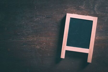 Small A-frame black board with blank area for text or message on rustic wood table with low key scene and vintage filter effectの写真素材