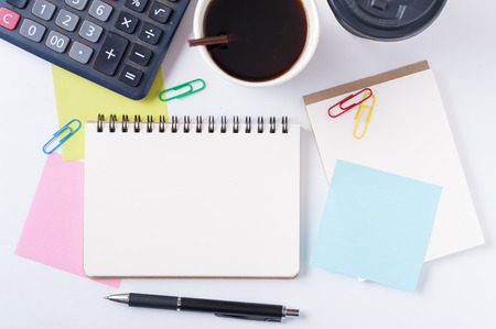 Opened notebook with blank space for text or message, sticky paper, calculator, and take away coffee cup on office tableの写真素材