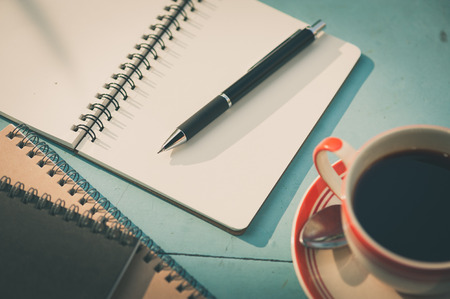Small notebook and pen beside coffee cup on blue wood table at outdoor area in cafe with morning...
