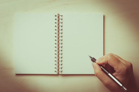 Male right hand writing on opened notebook with blank area for text or message and pen on wood table with vintage filter effectの写真素材