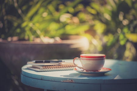 Coffee cup, notebooks, and pen on blue veteran table in morning time with vintage filter effectの写真素材
