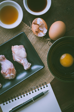 Preparation for cooking in home kitchen. Chicken wings in ceramic dish and ingredients on wood table with vintage filter effect.の写真素材