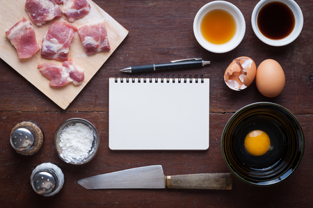 Preparation for cooking in home kitchen. Soft pork ribs on chopping board, notepad for check list, egg, and ingredients on wood table.の写真素材