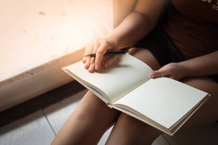 Young woman reading blank book while sitting beside window in morning time on weekend. Morning lifestyle on weekend concept.の写真素材