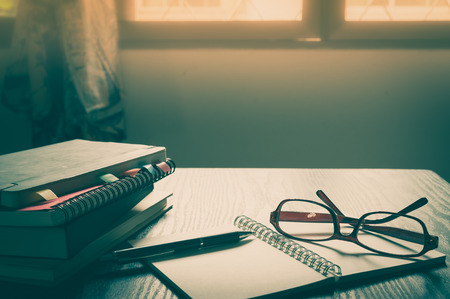 Glasses put down on table beside notebooks and pen in morning time on work day. Freelance business working concept with vintage filter effectの写真素材