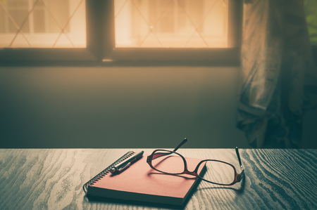 Notebook, pen, and glasses on working table in morning time on work day. Freelance business working concept with vintage filter effectの写真素材