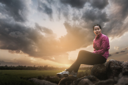 Vacation lifestyle scene of woman wearing sport cloths sitting on rocks with nature view in blurry background in morning time. Woman activity on holiday conceptの写真素材