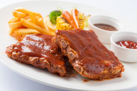 American style barbecue ribs steak with french fries, grilled vegetables, pepper sauce, and ketchup in ceramic dishの写真素材