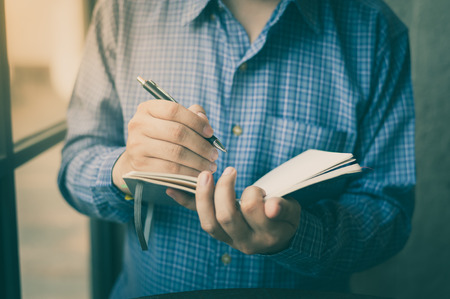 Adult freelance businessman writing on small notebook in cafe on weekend morning. Business lifestyle on weekend concept with vintage filter effectの写真素材