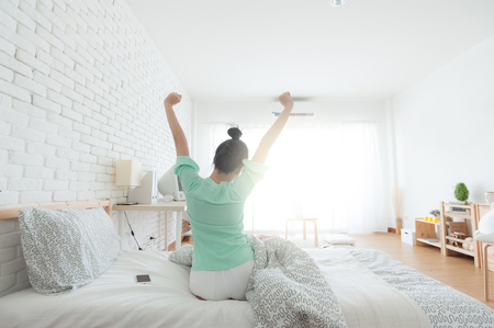 Young attractive Asian woman wear green casual cloths stretching after wake up on bed. Lazy girl activity on sunday morning.