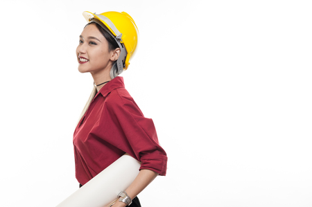 Young Asian woman architect with red shirt and yellow safety helmet smiling while carrying blueprint papers. Industrial occupation people conceptの写真素材