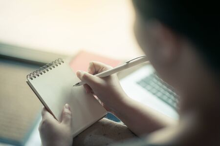 Woman hand writing some idea on small notepad while sitting on chair in house. Freelance working from anywhere concept with vintage filter effectの写真素材