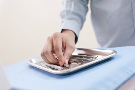 Male hand touching dental instrument on metal trayの写真素材