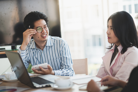 Young Asian businessman and businesswoman talking about their work while looking at laptop monitor in meeting room. Startup business for freelance workers conceptの写真素材