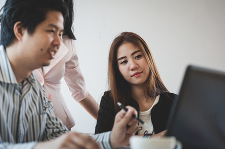 Young Asian businessman and businesswoman talking about their work while looking at laptop monitor in meeting room. Startup business for freelance workers conceptの写真素材