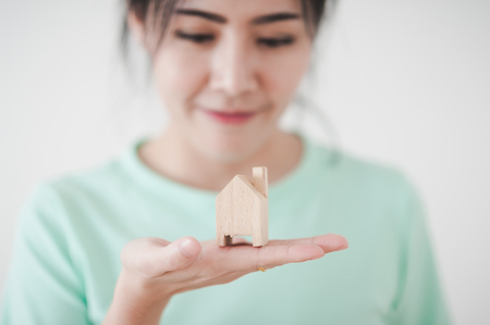 Young attractive Asian woman showing small wood house model in her hand. Business, life growth, and dream plan for family conceptの写真素材