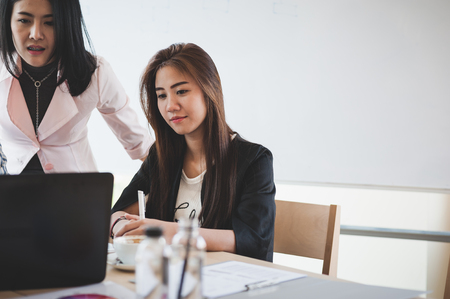 Two Asian businesswomen discussing about their project while participating in company meeting. Young startup businesspeople brainstorm and teamwork conceptの写真素材