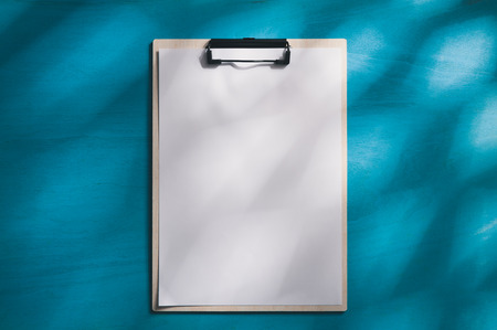 A4 size clipboard with white paper on blue wood table with natural lighting effect in morning time. background with blank area for text or message.の写真素材
