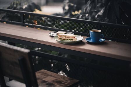 Abstract scene of breakfast meal set including tuna sandwich, hot long black coffee, and brownie cheese cake on outdoor wood bar.の写真素材