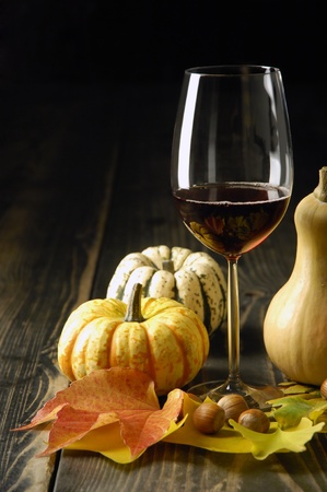 Autumn theme; pumpkins, leaves, glass of red wine and hazelnuts on rustic surfaceの写真素材