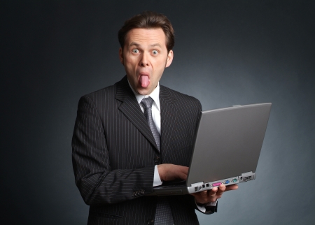 Businessman with laptop streching out his tongueの写真素材