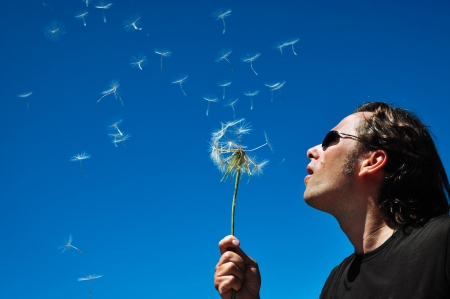 Man blowing a dandelion against blue sky, selective focusの写真素材