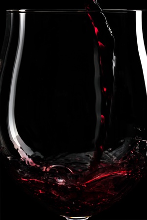 Close-up of red wine splashing into a glass infront of black background, selective focusの写真素材
