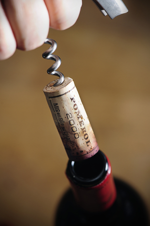Opening a wine bottle "Pomerol 2000", Hand pulling a cork on a corkscrew off the bottle, Pomerol is the famous vine planting area in France for Bordeaux wine, selective focusの写真素材