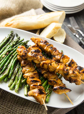 Grilled chicken skewers with green asparagus in a white plateの写真素材