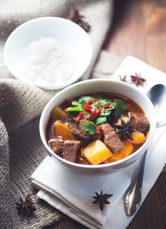 A bowl of Vietnamese beef stew with potatoes and garnishes on a white napkin and dark wooden undergroundの写真素材