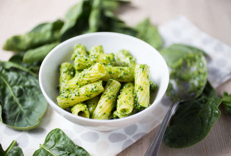 Closeup of a white bowl of pasta with green pesto and leaves scattered aroundの写真素材