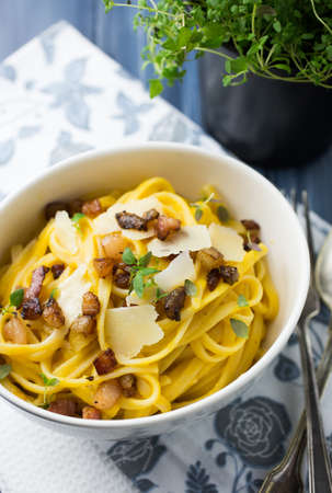 A white bowl of spaghetti carbonara and bacon topped with parmesan cheese on a blue gray backgroundの写真素材