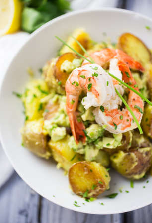 Bowl of potato salad with avocado and garlic mayo topped with prawns and chivesの写真素材