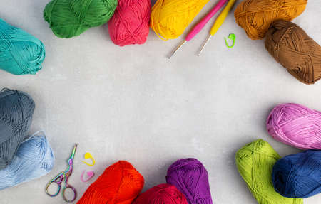 Colorful skeins of yarn, crochet hooks, stitch markers and crafting scissors arranged in a border...