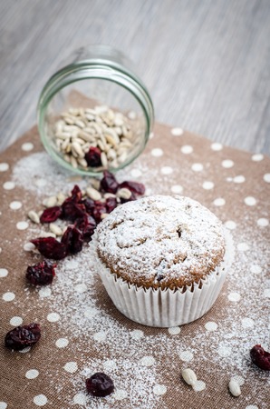 banana muffin with sunflower seeds and dried cranberries on a napkin with polka dots on wooden table, selective focusの写真素材