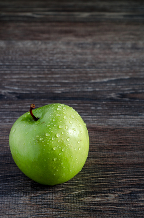 Fresh green apple with water droplets on a wooden tableの写真素材