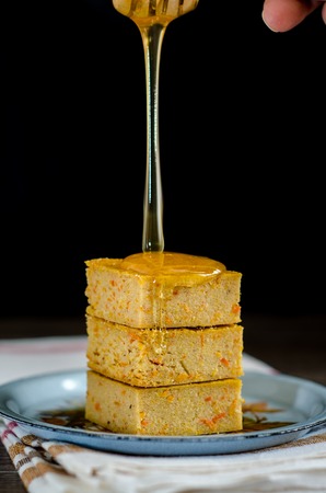 Tower of square pieces of cheese casseroles with honey dripping from a spoon on a black background....