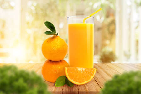 Fresh glass of orange juice, stack of Orange with leaves on wooden on warm light. Nature drinks.の写真素材