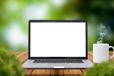 Laptop with blank screen on Wooden table with, coffee mug with smoke, blurred nature green...